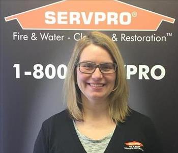 Female employee with blonde hair smiling in front of a SERVPRO black banner