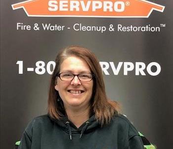 Female employee with reddish brown hair smiling in front of a SERVPRO black banner