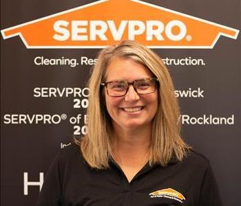 Female employee with blonde hair smiling in front of a SERVPRO black banner