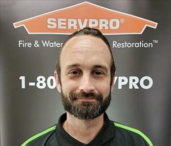 Male employee with dark hair smiling in front of a SERVPRO black banner