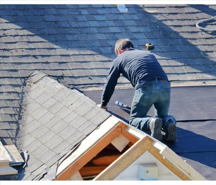 A roofer uses a nail gun to apply tarp to a roof in preparations for shingling.